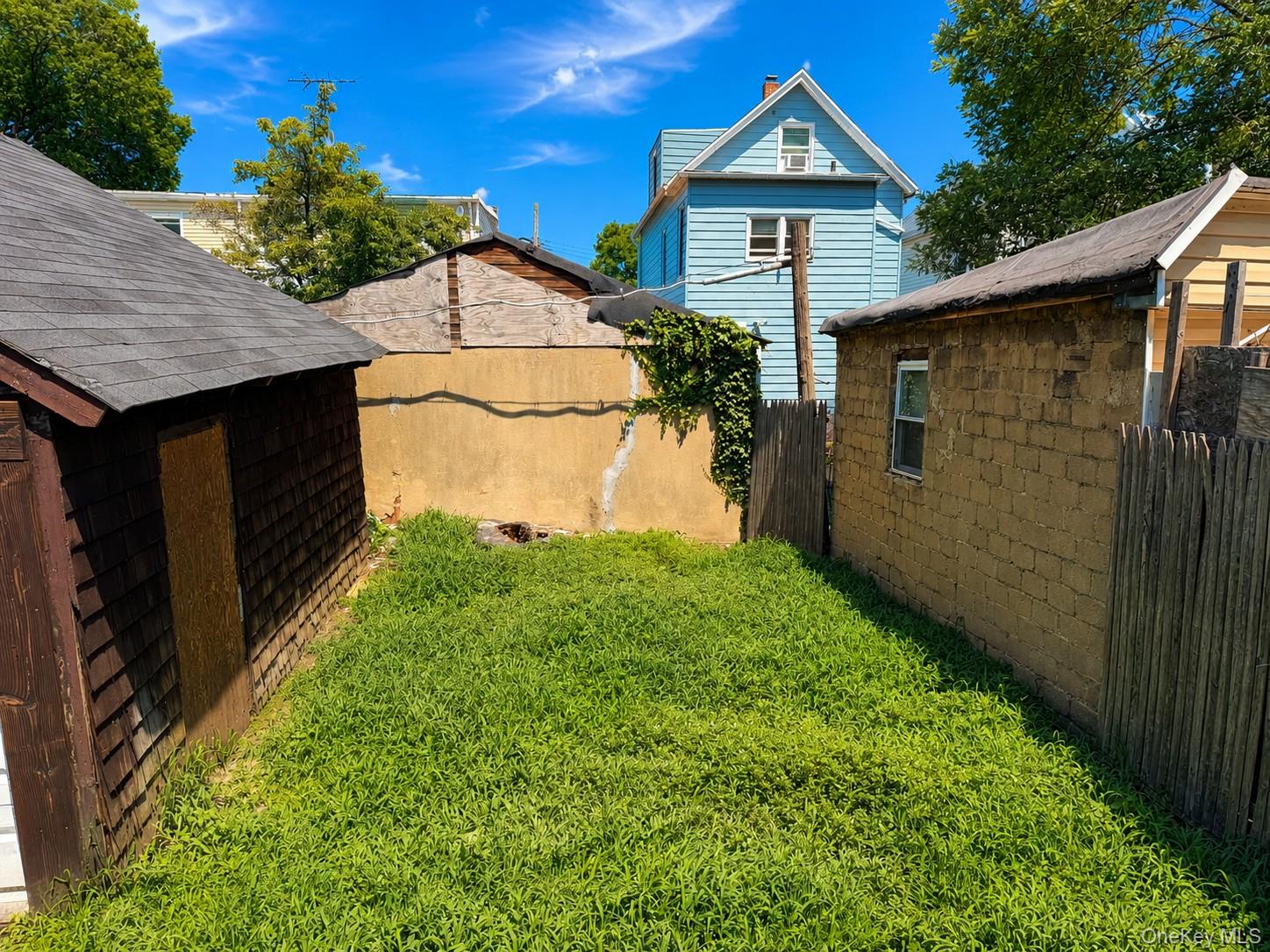 25 Monroe Street, Unit 1 Mount Vernon, NY 10550 - Photo 10 of 11 Grassed yard area featuring a shingled shed, privacy fencing, and a stucco wall