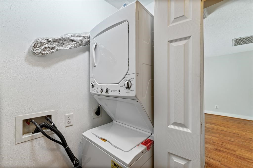 1305 Idylwild Street Houston, TX 77009 - Photo 29 of 31 This photo shows a compact laundry area with a stacked washer and dryer unit, neatly enclosed in a closet with bi-fold doors, adjacent to a room with wood flooring.