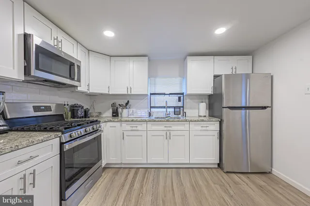 a kitchen with stainless steel appliances granite countertop a stove top oven a refrigerator white cabinets and wooden floor