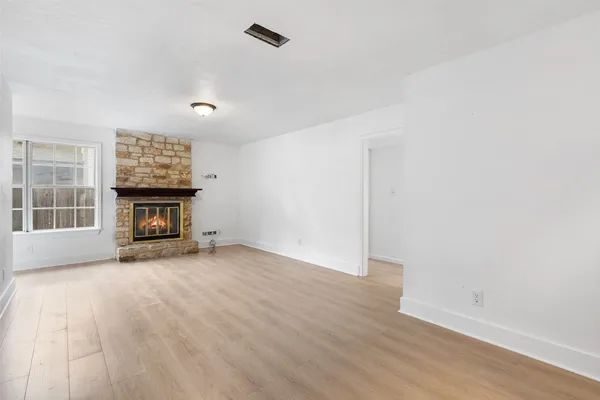 an empty room with wooden floor fireplace and windows