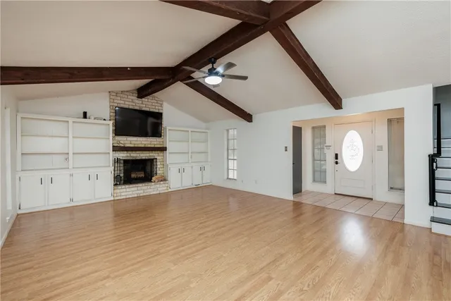 a view of an empty room with wooden floor fireplace and a window