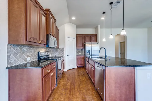 a kitchen with stainless steel appliances granite countertop a sink a stove and a wooden floors