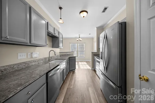 a kitchen with granite countertop a refrigerator a sink dishwasher a stove and white cabinets with wooden floor