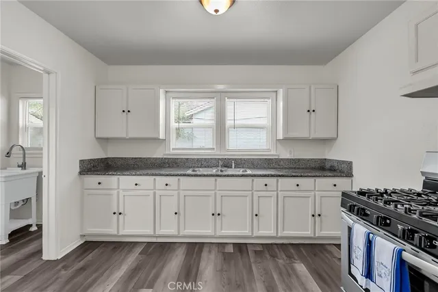 a kitchen with granite countertop white cabinets and a stove with wooden floor