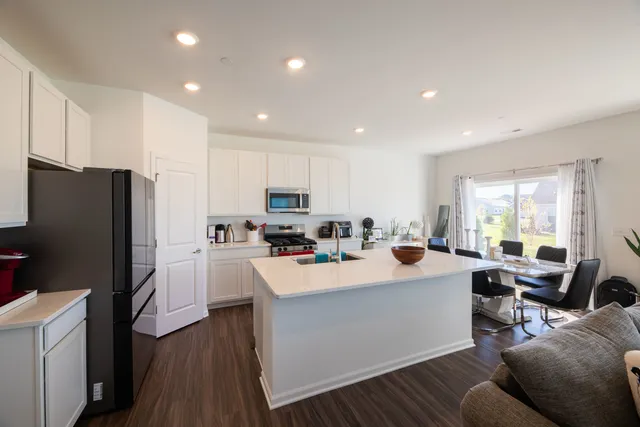 a kitchen with stainless steel appliances a stove a refrigerator a sink dishwasher and a dining table with wooden floor