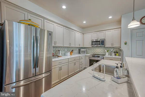 a kitchen with granite countertop stainless steel appliances a refrigerator a stove top oven and white cabinets