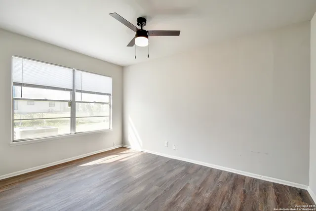 an empty room with wooden floor fan and windows