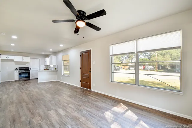 a view of an empty room with a window and kitchen view