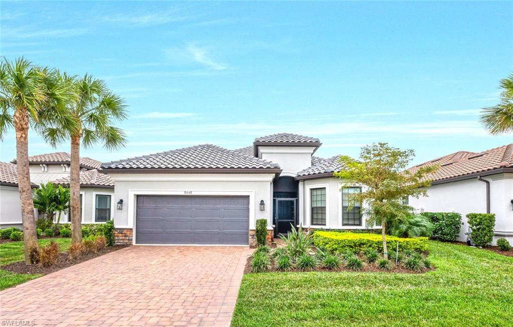 Contemporary stucco exterior featuring a tiled roof, paver driveway, an attached garage, and mature landscaping