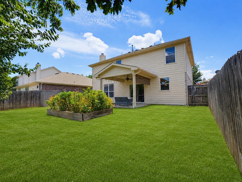 13268 Fencerow Road Fort Worth, TX 76244 - Photo 21 of 25 Expansive backyard featuring a covered patio, a raised garden bed with established plantings, a full privacy fence, and a generous lawn area