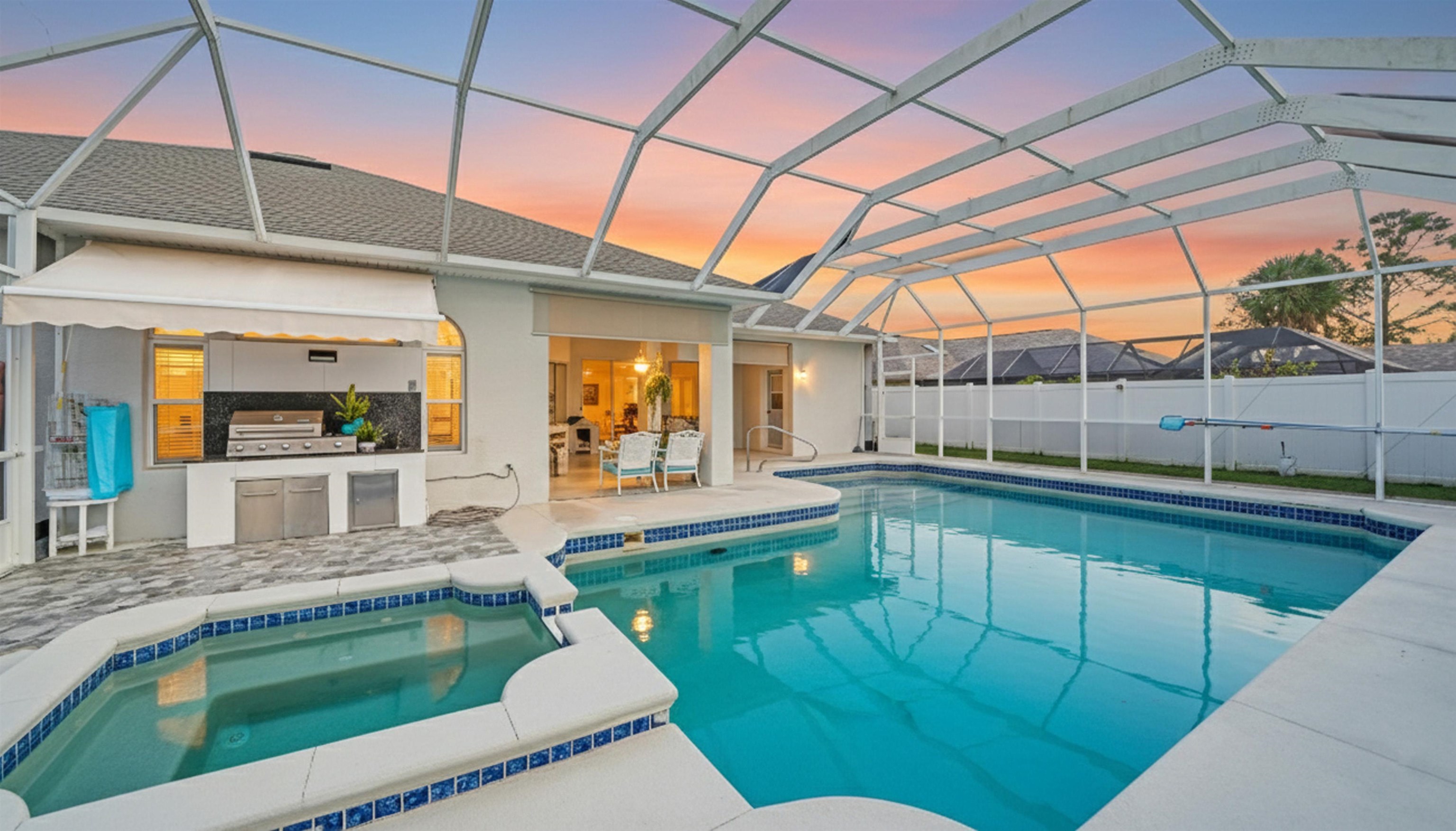 22 Flanders Lane Palm Coast, FL 32137 - Photo 3 of 70 Pool at dusk with glass enclosure, a sunroom, a pool with connected hot tub, a patio area, and exterior kitchen