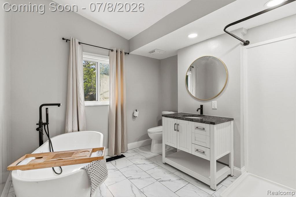 5698 McGrandy Road Bridgeport, MI 48722 - Photo 20 of 26 Bathroom featuring a freestanding soaking tub with a matte black floor-mounted faucet, white vanity with a dark countertop and undermount sink, and a circular mirror