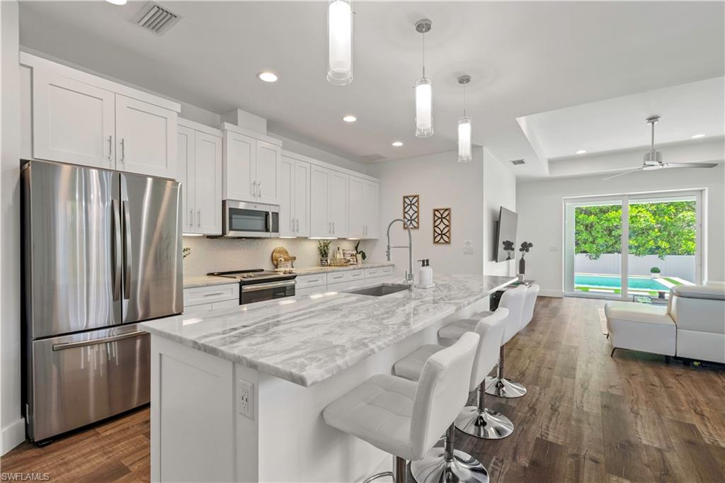 1100 Steeves Avenue Naples, FL 34104 - Photo 38 of 38 a kitchen with granite countertop a refrigerator a stove a sink a dining table and chairs with wooden floor