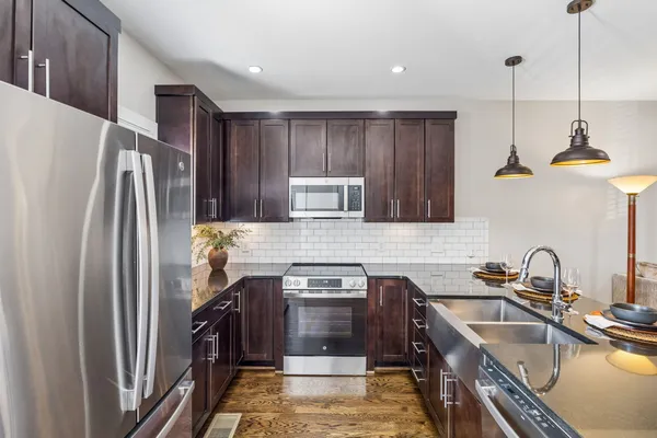 a kitchen with stainless steel appliances granite countertop a refrigerator a sink dishwasher a stove and a oven with wooden floor