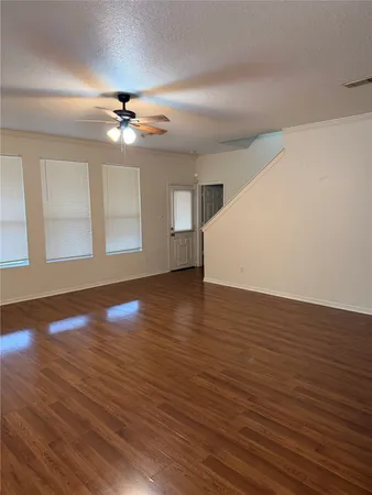 a view of an empty room with wooden floor and a ceiling fan