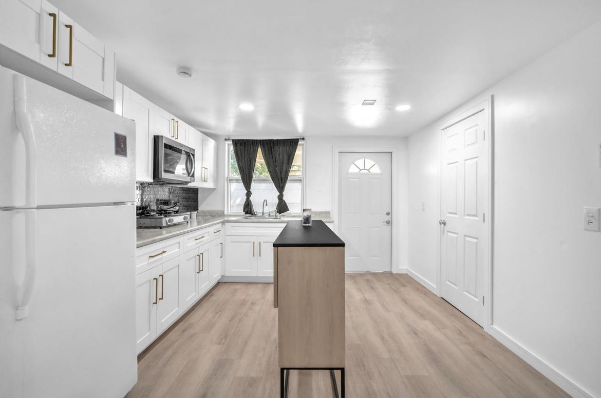 7151 Taft Street, Unit REAR Hollywood, FL 33024 - Photo 3 of 8 a kitchen with granite countertop a refrigerator oven a sink dishwasher and white cabinets with wooden floor