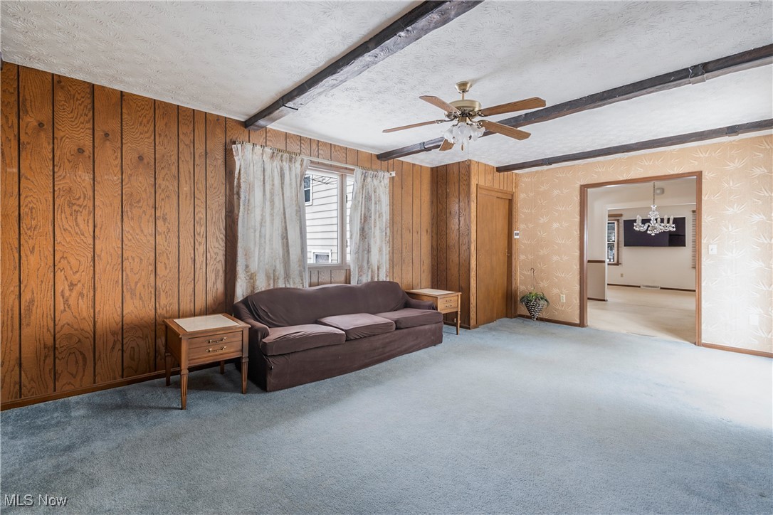 4875 New Road Youngstown, OH 44515 - Photo 16 of 25 Living room with a textured ceiling, ceiling fan with notable chandelier, wood walls, and beamed ceiling