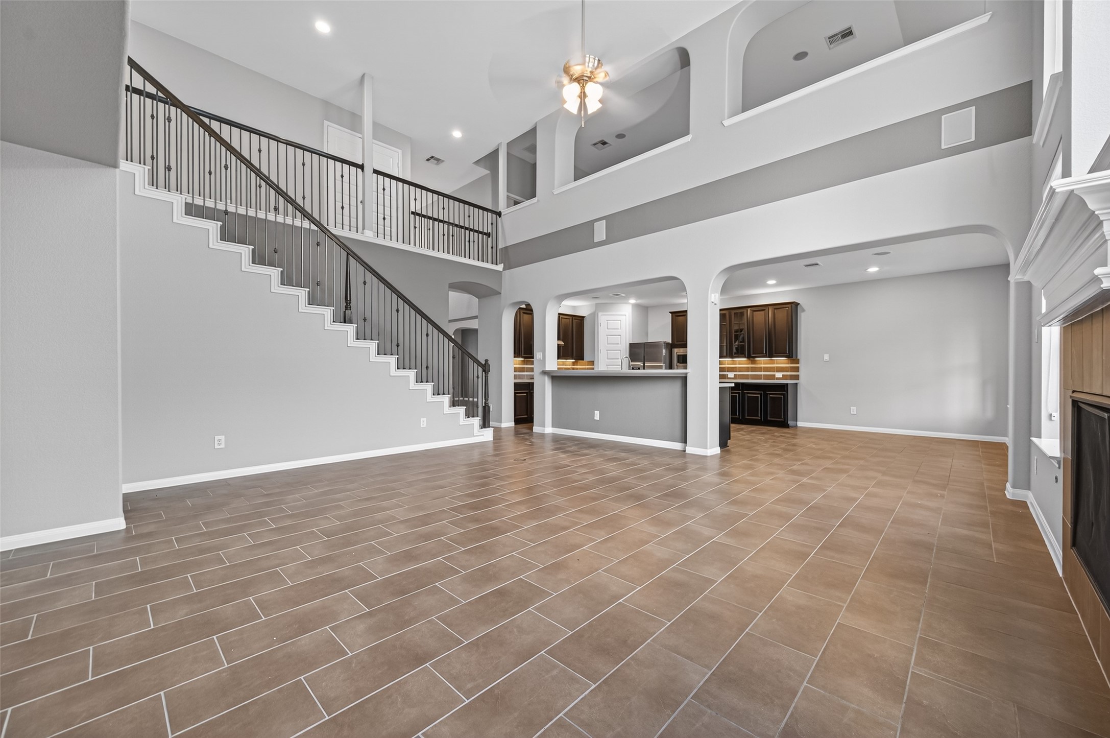 7003 Bristol Memorial Drive Spring, TX 77379 - Photo 15 of 40 Expansive two-story living room in this Spring TX 77379 home featuring soaring ceilings, dramatic stacked windows, and abundant natural light. The open-concept layout flows seamlessly into the kitchen, creating an ideal space for entertaining and everyday living. A central fireplace anchors the room, while durable tile flooring enhances both style and function. Upper-level overlooks add architectural dimension and openness.