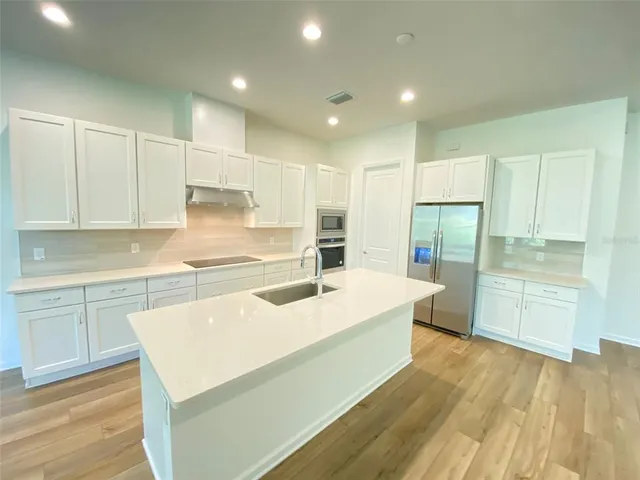 a kitchen with a sink a stove a refrigerator and white cabinets with wooden floor