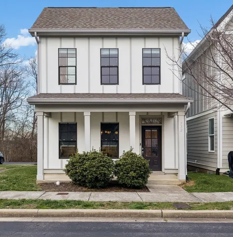 a view of a white house with a yard plants and large tree