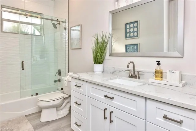 a bathroom with a granite countertop sink a toilet a mirror a vanity and shower