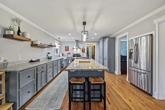 a kitchen with stainless steel appliances granite countertop a refrigerator a sink dishwasher a stove and a dining table with wooden floor