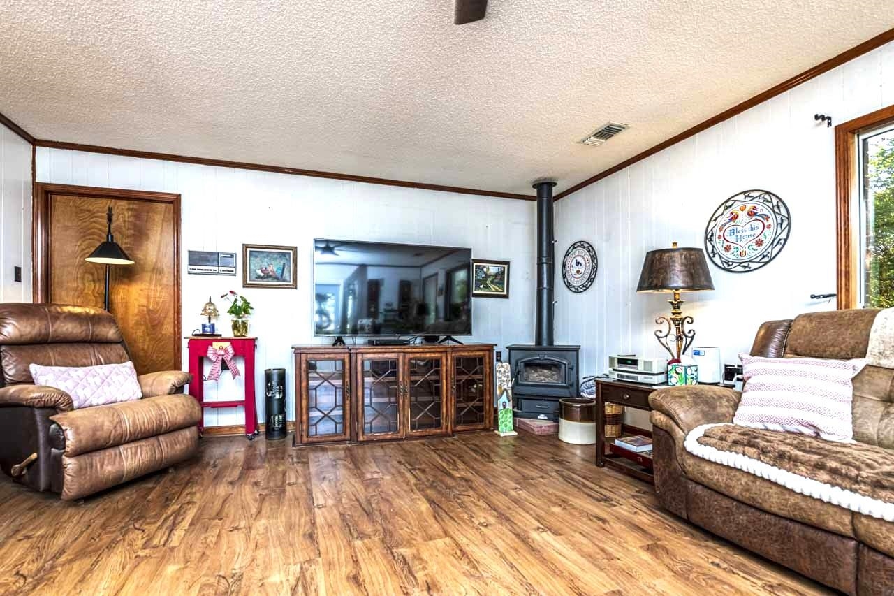 937 Kelleys Chapel Road Burlison, TN 38015 - Photo 5 of 40 Living room with crown molding, wood finished floors, a textured ceiling, a wood stove, and ceiling fan