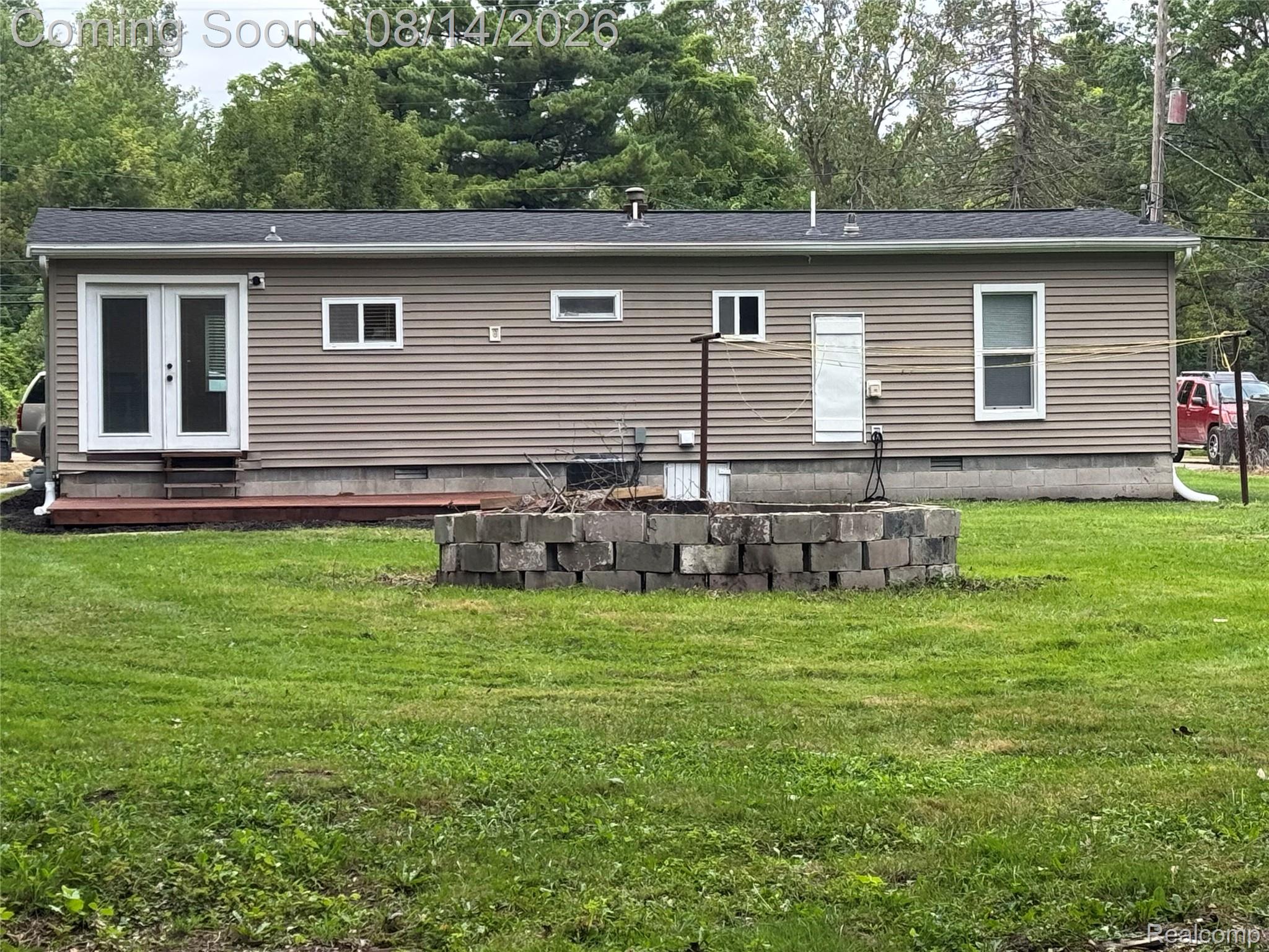 Exterior featuring horizontal siding, white-framed windows, a dark shingle roof, a rear deck, and a stone fire pit