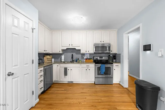 a kitchen with stainless steel appliances a stove top oven a refrigerator a sink and dishwasher with white cabinets