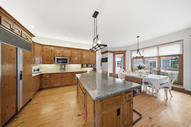 a kitchen with granite countertop kitchen island stainless steel appliances a dining table chairs sink and white cabinets