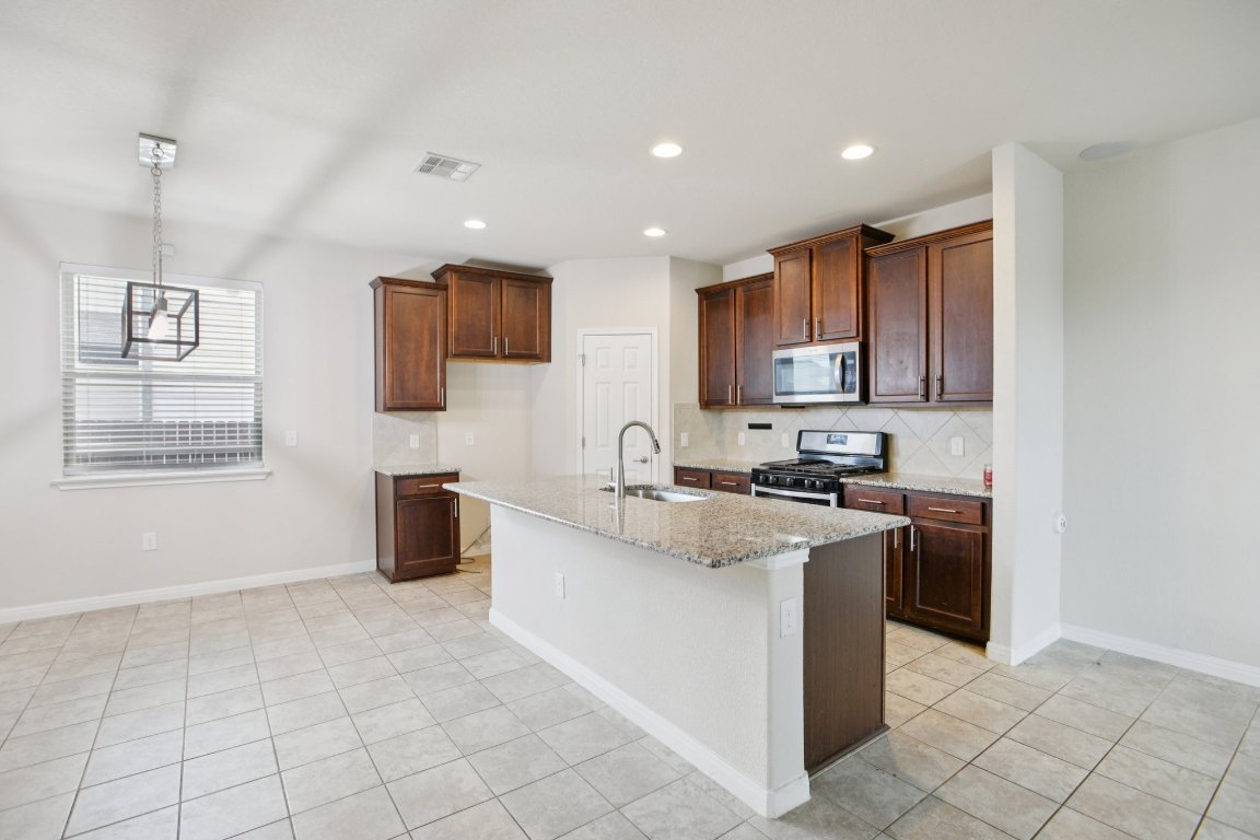 176 Mayney Ln. Leander, TX 78641 - Photo 10 of 34 Kitchen featuring light stone counters, appliances with stainless steel finishes, an island with sink, decorative backsplash, and recessed lighting