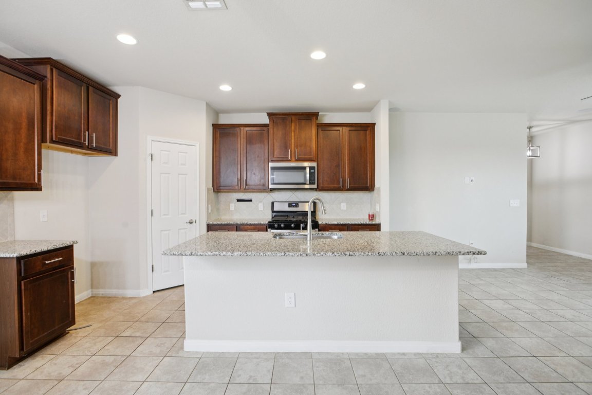 176 Mayney Ln. Leander, TX 78641 - Photo 12 of 34 Kitchen featuring light stone counters, stainless steel appliances, a kitchen island with sink, decorative backsplash, and recessed lighting