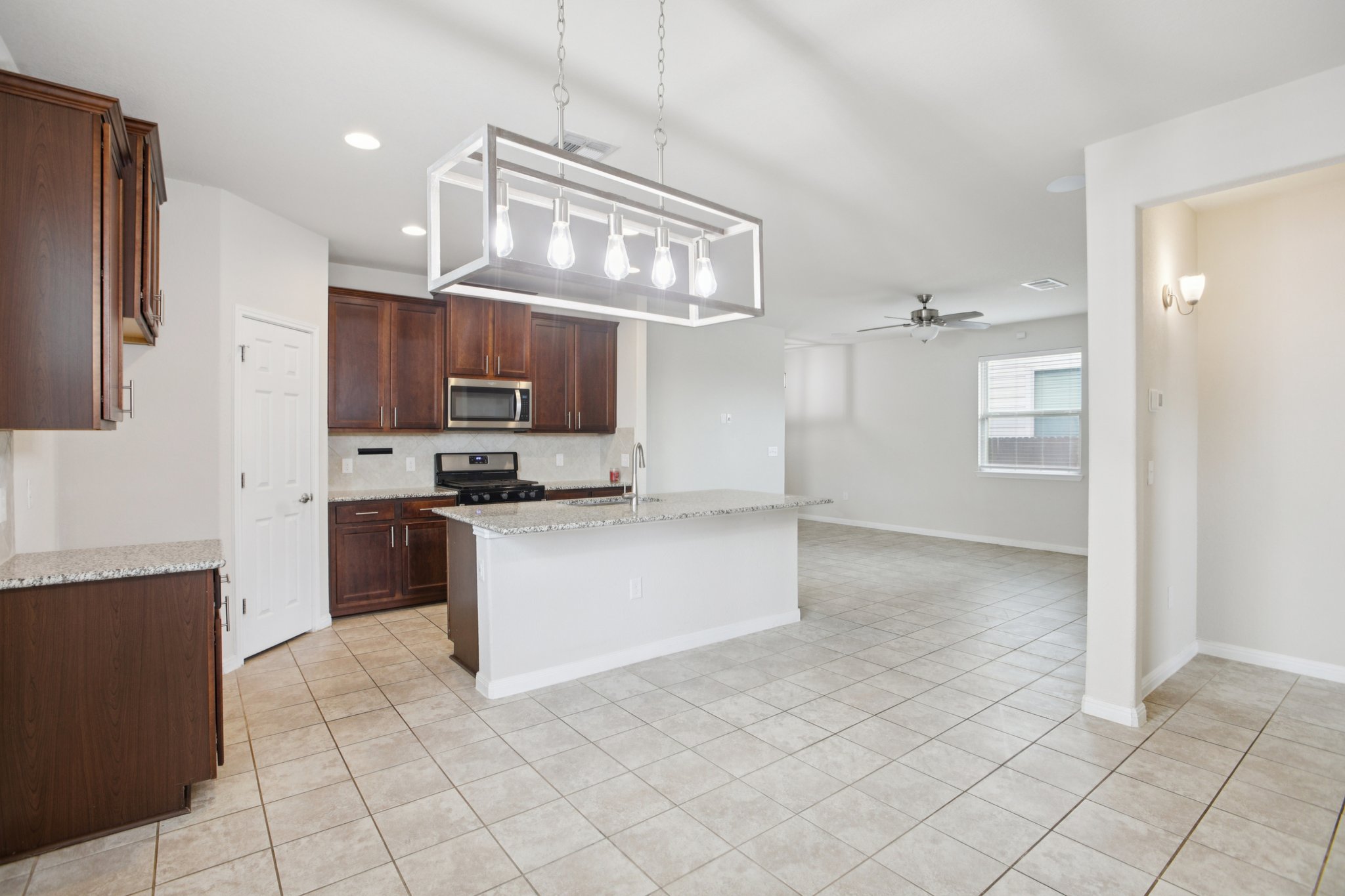 176 Mayney Ln. Leander, TX 78641 - Photo 16 of 37 Kitchen featuring light stone counters, hanging light fixtures, an island with sink, black range with gas cooktop, and stainless steel microwave