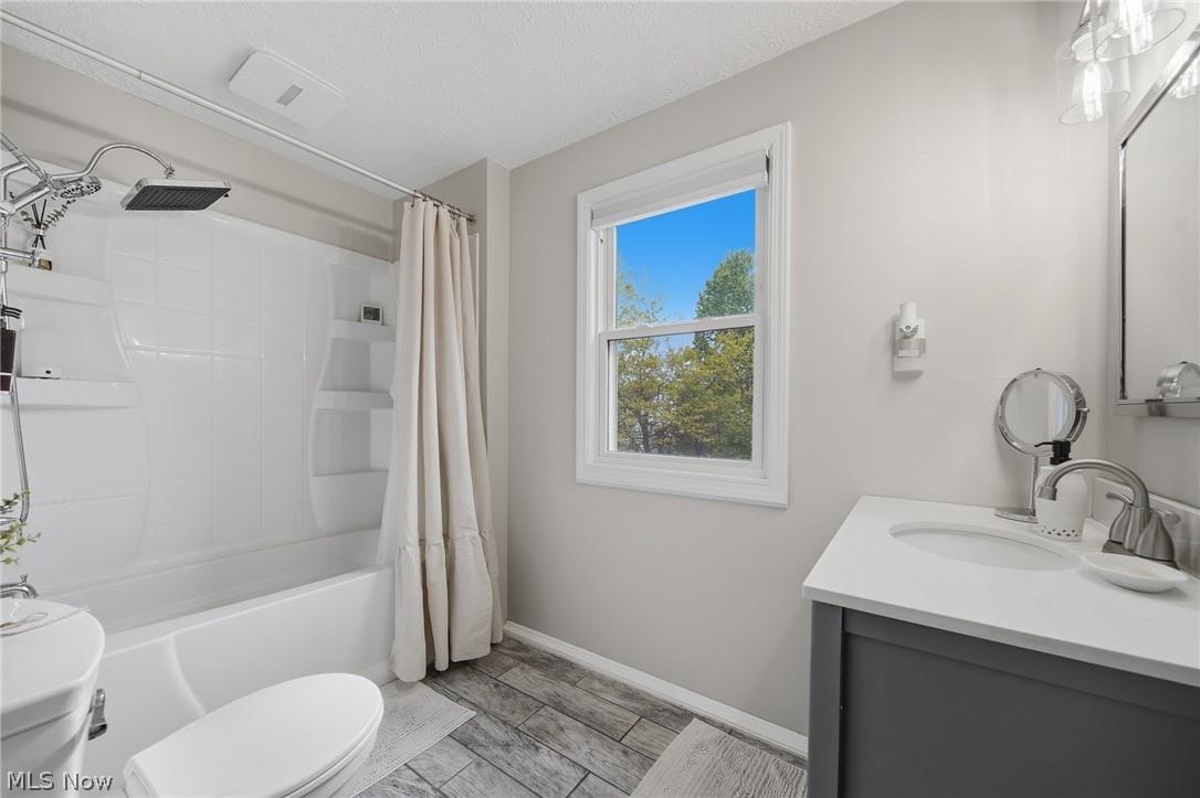 2231 Brockway Road University Heights, OH 44118 - Photo 24 of 46 Full bathroom featuring a white tub and shower combination with a rainfall showerhead, a single window, a dark gray vanity with a white countertop and integrated sink, and wood-finish flooring
