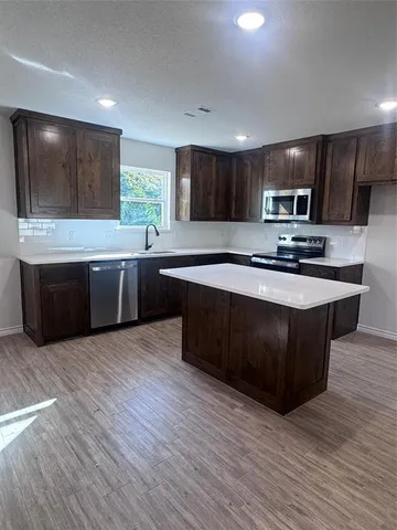 a kitchen with stainless steel appliances granite countertop a sink wooden cabinets and a wooden floor