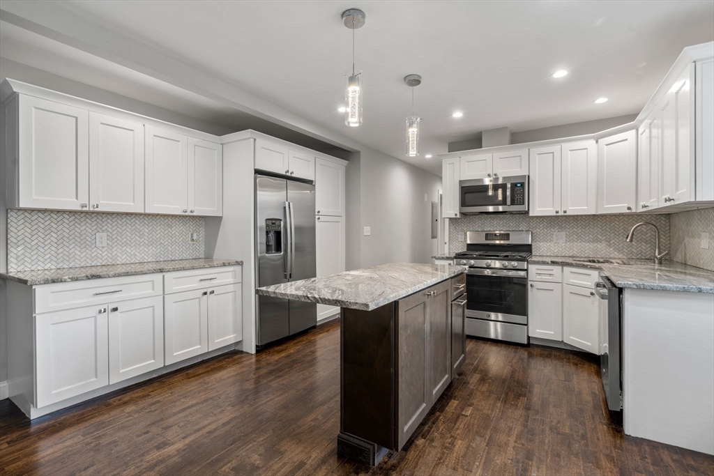 a kitchen with kitchen island granite countertop stainless steel appliances cabinets a sink and wooden floor