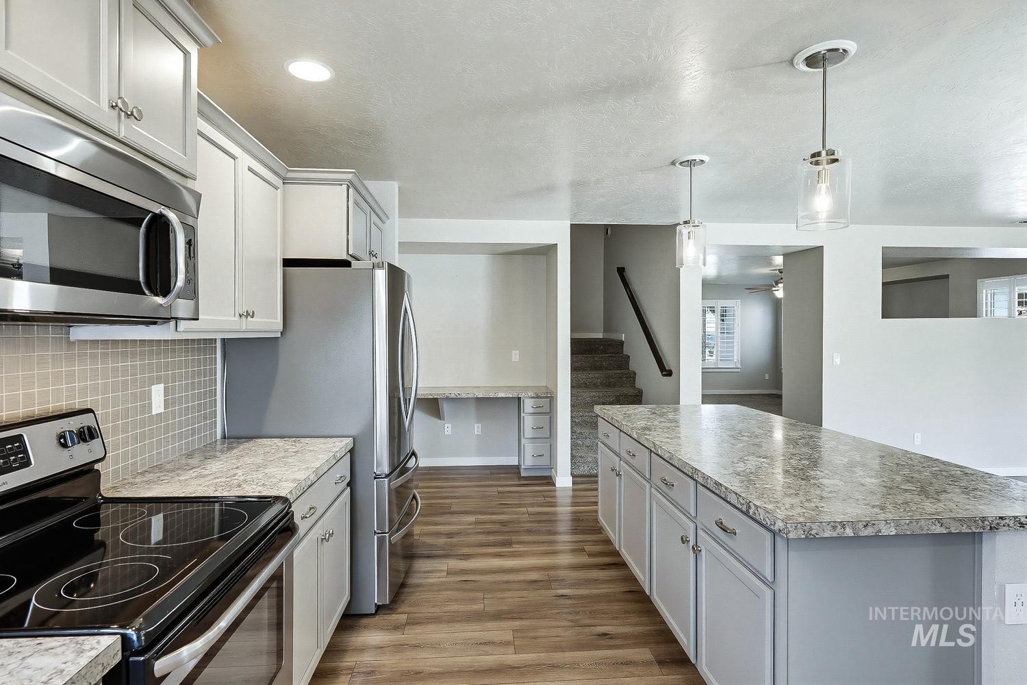 846 North Hidden View Way Star, ID 83669 - Photo 14 of 49 Kitchen featuring a long island with a light-toned countertop, wood-finish flooring, light grey cabinetry, stainless steel appliances, and a tiled backsplash