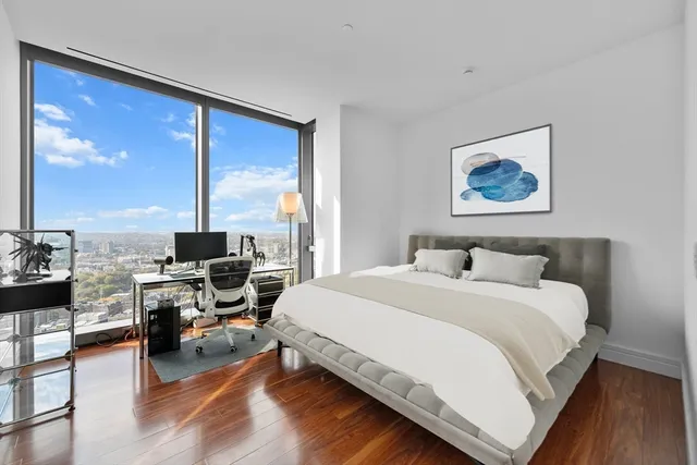 a bedroom with a bed a large window and wooden floor