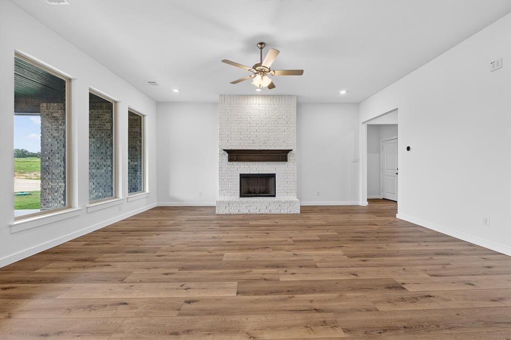416 McAlpine Drive Springtown, TX 76082 - Photo 9 of 40 Spacious living area featuring wood-finish flooring, a white brick fireplace with a dark wood mantel, and a ceiling fan