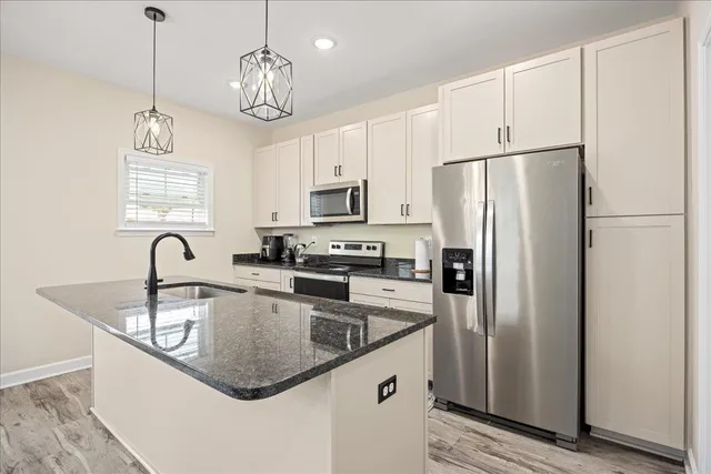 a kitchen with stainless steel appliances granite countertop a refrigerator a sink dishwasher a stove and a dining table with wooden floor