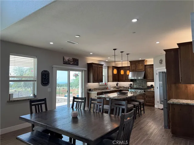 a kitchen with stainless steel appliances granite countertop a stove a refrigerator a sink a dining table and chairs with wooden floor