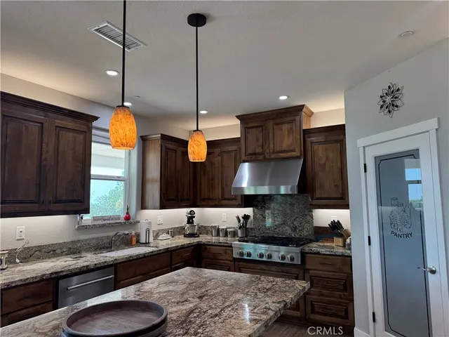 a kitchen with stainless steel appliances kitchen island granite countertop a refrigerator a stove and a wooden floor
