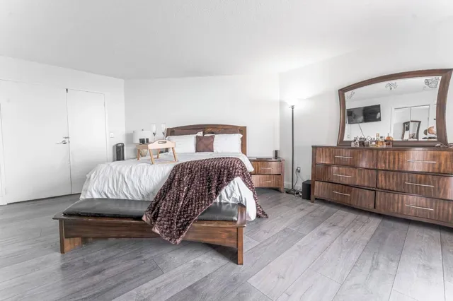 a bedroom with a bed and dresser with wooden floor