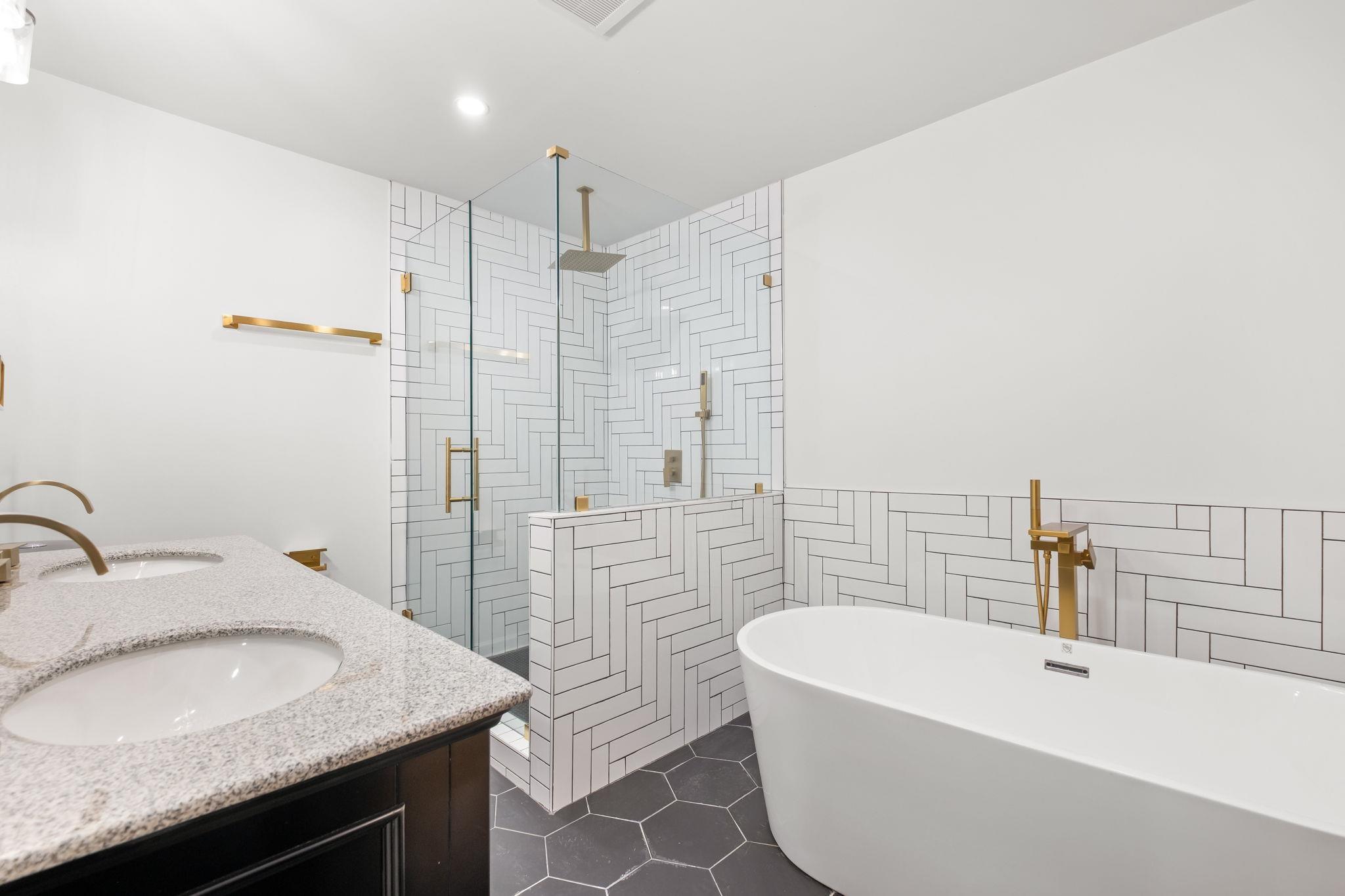Bathroom with a shower stall, a freestanding tub, tile walls, double vanity, and dark tile patterned floors