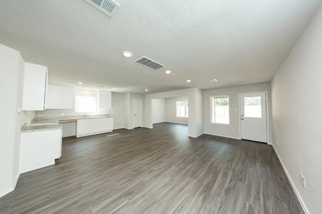 a view of empty room with wooden floor and kitchen