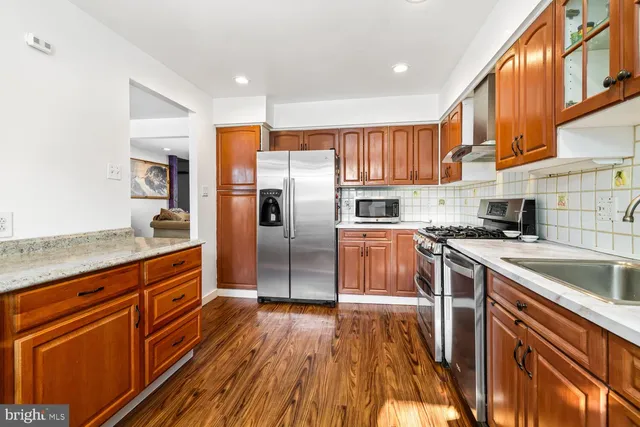 a kitchen with stainless steel appliances granite countertop a refrigerator a sink dishwasher a stove and white countertops with wooden floor