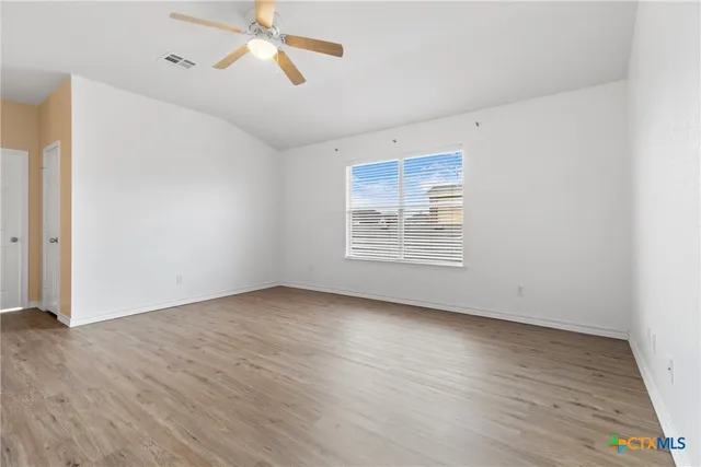 an empty room with wooden floor ceiling fan and windows