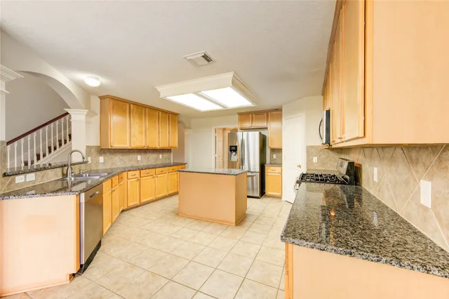a large kitchen with granite countertop a large counter top cabinets and stainless steel appliances