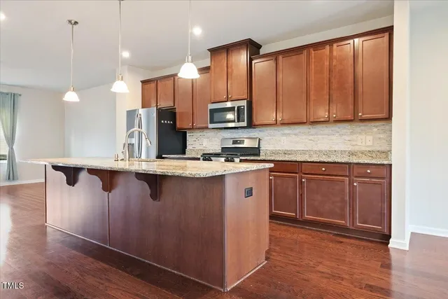 a kitchen with kitchen island granite countertop wooden cabinets a refrigerator and wooden floor