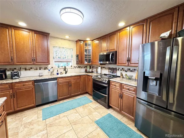 a kitchen with stainless steel appliances granite countertop a refrigerator a stove a sink dishwasher and wooden cabinets